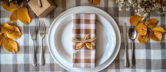 Autumn table setting with oval plates cutlery checkered napkin gift box and dry leaves ideal for seasonal gatherings and celebrations