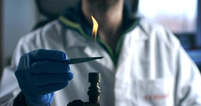 Super slow motion close up of scientist carefully sterilizes pair of tweezers with fire in a lab with precision and focus required for research before preparing for biochemical analysis at 1000 fps.