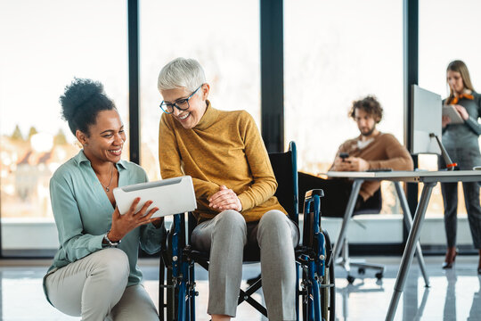 Disabled woman in wheelchair looking at computer, discussing startup project with interracial team - Powered by Adobe