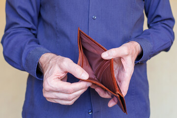 Man in blue shirt holds empty brown wallet in his hands. Selective focus.