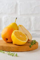 Fresh pear with lemon and thyme on a wooden board on a light background. Vertical orientation.