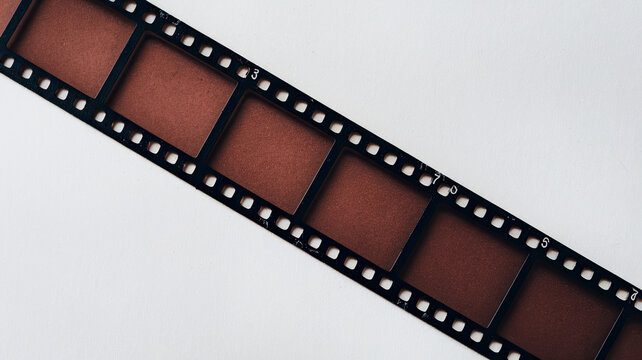 A diagonal film strip with rectangular frames and perforated edges on a white background, featuring a dark reddish-brown tint and vertical orientation of frames and numbers.