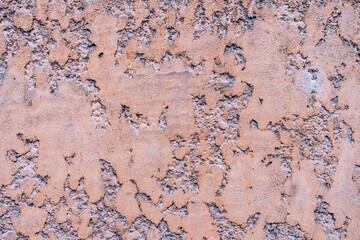 A close-up of a textured wall with peeling plaster and rough, uneven surfaces in earthy tones of orange and gray. The weathered look creates an abstract, aged pattern ideal for backgrounds or projects