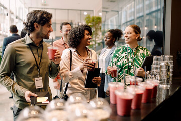 Smiling male and female business entrepreneurs enjoying drinks during break time at convention center
