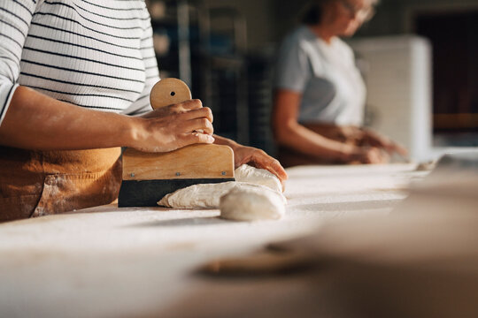 Midsection of female baker cutting dough with cutter while working at bakery