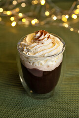 Coffee with whipped cream and spices in a glass with double walls on a bokeh background.