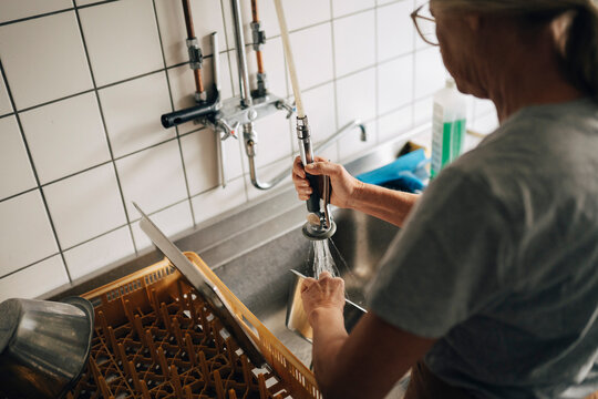 High angle view of senior female baker spraying water on dishes while working in commercial kitchen