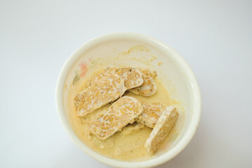Raw tempeh that has been cut in a white bowl containing dough, with a white background.