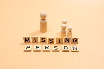 A group of people made of wooden figures. The group stands in front of a sign saying Missing...