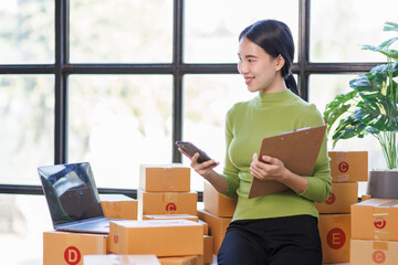 Asian business woman on sofa using a laptop computer checking customer order online shipping boxes at home. Starting SME Small business entrepreneur freelance. Online business, SME Work home concept.
