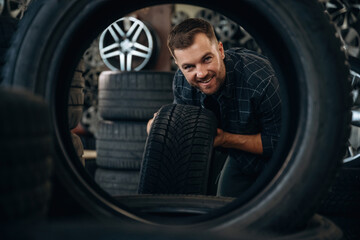 Looking through the hole in tire. Man worker is maintenance station with wheels