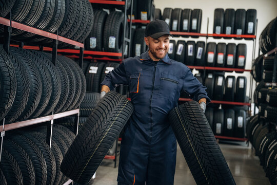 Walking and holding the tires. Man worker is maintenance station with wheels