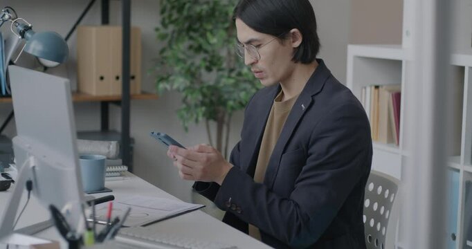 Asian businessman taking photo of document using smartphone camera sharing information online in office. Modern technology and business concept.