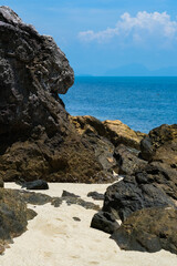 A rocky beach on Koh Samui, Thailand, featuring rugged volcanic rocks, soft sand, and a turquoise sea.