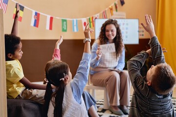 Back view of children raising hands while enjoying English lesson in primary school classroom copy space