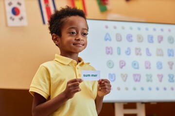Waist up portrait of smiling young African American boy holding word flashcard in primary school...