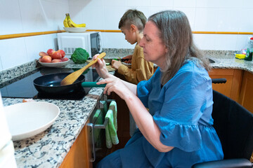 Woman in wheelchair cooking with her grandson in the kitchen