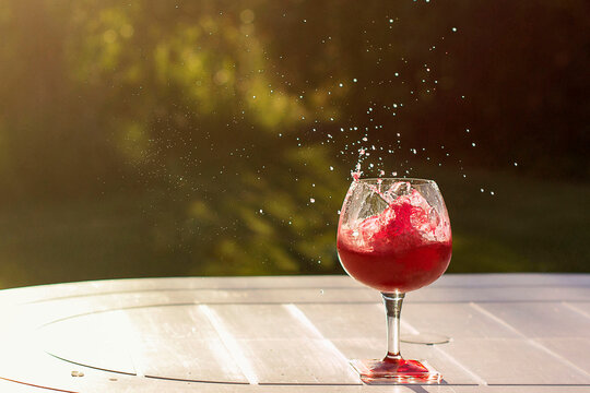 Close-up of a ice cubes splashing into a glass of Red wine on a garden table in summer