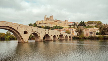 Naklejka premium Pont en pierre enjambant un fleuve avec vue vue sur Bézier et la cathédrale