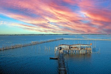 Obraz premium Wooden fish farm with a sunset sky over calm water, creating a serene landscape