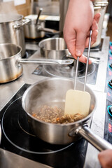chef's hand stirs a pot on a modern stove, steam rising from the contents. Various pots and pans are in the background, showcasing a busy kitchen environment. Perfect for cooking and culinary themes.
