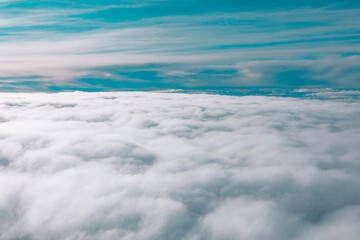 Vast expanse of clouds viewed from above from an airplane. Above the clouds, the sky is visible with a gradient of blue and gray tones, indicating varying weather conditions or the time of day