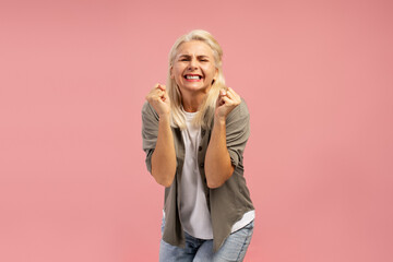 Excited woman shaking fists on pink background, celebrating success and achievement