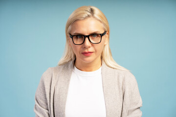 Serious blond woman wearing glasses posing on blue background