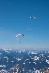 three paragliders circle over the Allgäu Alps in the blue sky