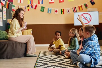 Wide angle side view of young woman teaching road safety rules to group of children sitting on...