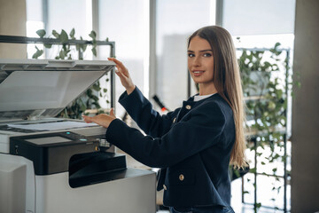 Working with printer. Beautiful woman is in the office