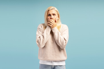 Shocked woman covering her mouth with hands on blue background