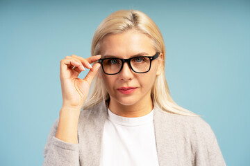 Confident businesswoman adjusting eyeglasses on blue background