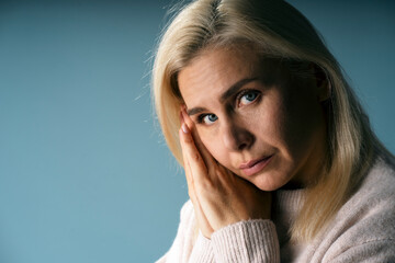 Fototapeta premium Sad woman holding face in hands on blue background
