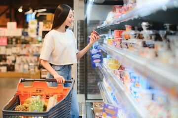 Smiling happy woman enjoying shopping at the supermarket, she is leaning on a full cart