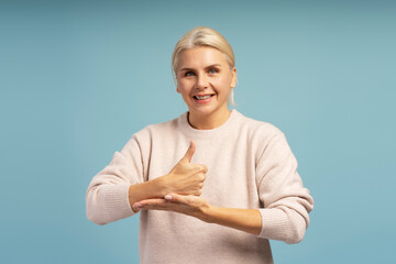 Smiling woman showing thumb up sign in sign language on blue background