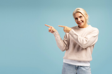 Smiling woman pointing to the left side on blue background