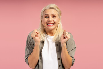 Excited mature woman celebrating success on pink background