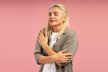 Serene mature woman embracing herself on pink background