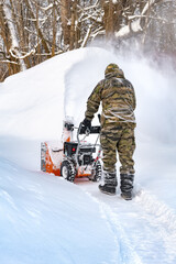 The self-propelled snow-plough blower. The man back to camera in warm clothes gloves instead of the big shovel has chosen a self-propelled engine snowplow outdoors