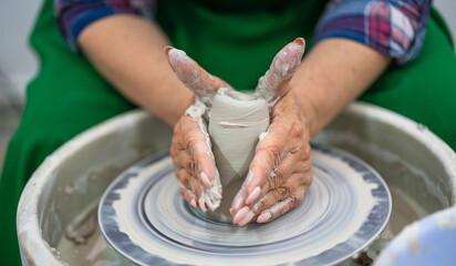 Hands shaping a clay vessel on a pottery wheel, surrounded by a messy workspace. The focus is on the craft and precision, highlighting the art of pottery making in a serene, creative environment.