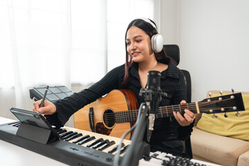 Professional Musician with condenser microphone and tablet for Mixing Mastering music. Music composer woman composing a song with guitar and piano keyboard at digital Recording home studio