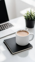 Coffee cup on a notebook beside a laptop with a plant at a tidy workspace