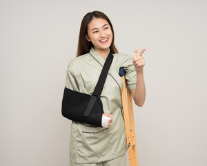 Happy young asian woman broken arm pointing finger on isolated background. Female put on plaster...