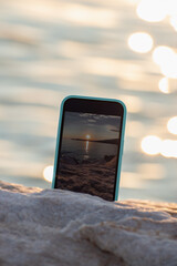 Mobile phone photographing, filming or recording video sunset over sea, blurred ocean water on background. Smartphone taking picture, creating travel content, summer trip, online blog