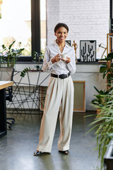 A young African American woman in a white shirt stands in a bright office holding a cup.