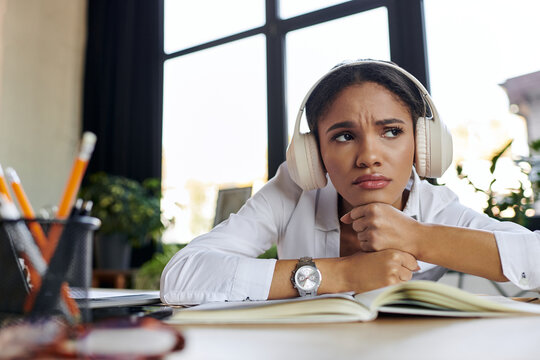 A young professional woman in a white shirt and headphones feeling sad in office - Powered by Adobe