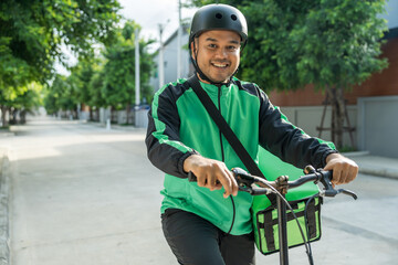 Portrait Rider food delivery man wearing green uniform and helmet cycling a bicycle the food service to customer. Happy delivery man with green backpack shipping of goods to customers.