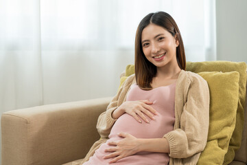 Happy pregnant woman caresses her belly while taking rest on sofa at home, concept of happy motherhood waiting for childbirth, family planning and pregnancy with insurance for child health.