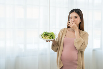 Unhappy young asian pregnant woman feeling with morning sickness to vegetable salad, frustrated...